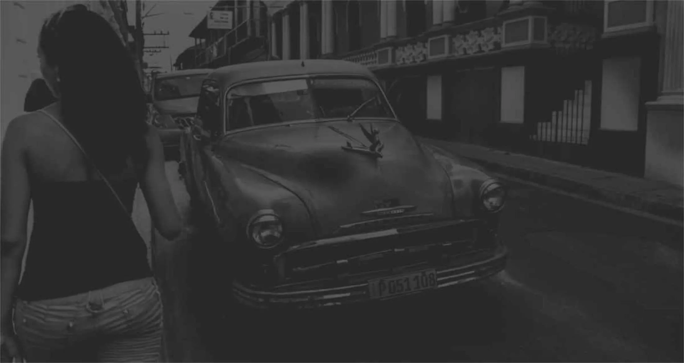 A Karelia walking down the street with an old car in Santiago de Cuba.